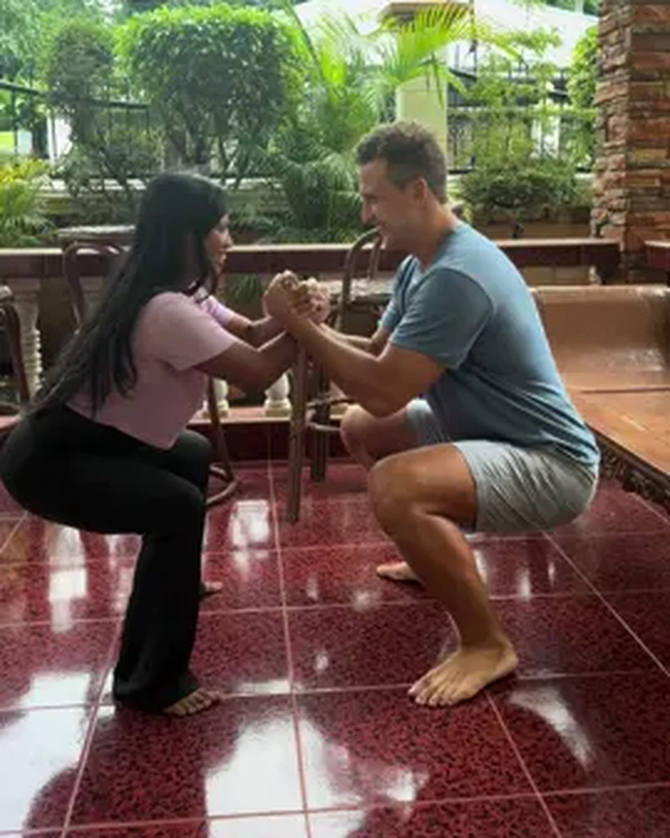 Video cover. Vivian and her partner squat face to face, holding hands on a tiled porch.