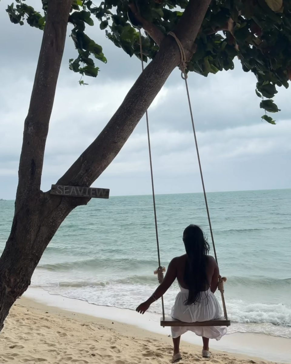 Vivian in a white dress on a rope swing over the sand, facing the sea.